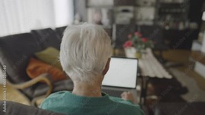 Slow motion - Backshot of a grandmother's gray hair, while she is annoyed while typing on her computer that is sitting on her lap, in a living room with leather seats, TV, windows, in daylight.