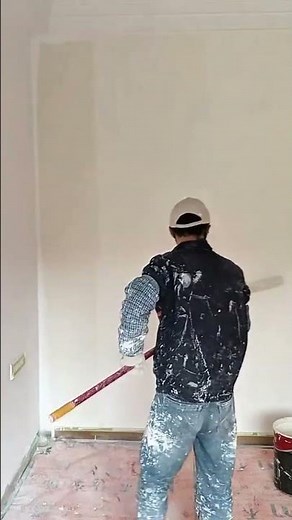 painting indoor white walls using a long handle roller brush to achieve a smooth and even surface