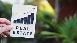 property value and return on investment or rent price, hand holding real estate sign with graph showing stats going up in front of backyard backyard and building exterior