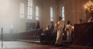 Liturgical in Grand Church: Majestic Procession Of Ministers And Priests Walking with Processional Cross. Congregation Stands In Reverence, Christians Rejoice In Ceremony of Mass in The Lord's Glory