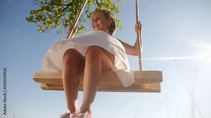 little girl kid swinging on a wooden swing on a tree in the park. happy family kid dream concept. little kid girl playing on wooden swing on tree dream fun concept in park