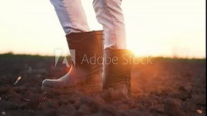 Agriculture. Farmer in rubber boots walks across a black field. Farm worker in rubber boots. Feet in rubber boots step on soil in field. Farmer works on land at farm. Fertile soil on a rural farm