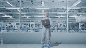 Full Body Of Asian Male Scientist Typing On A Laptop And Looking Around In Modern Lab Factory with Automated Robots