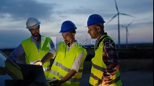 Engineers teamwork people working on laptop computer discussing renewable energy project at wind turbine farm -