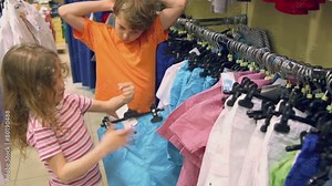 Little girl tries on shorts and her brother watches in clothes shop