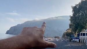 KAMARI - SANTORINI Oggi ci troviamo a Kamari, non potevo di certo perdermi questo angolo di Santorini. Ma cosa sappiamo di Kamari? Kamari è una delle località balneari più conosciute di Santorini, situata sulla costa sud-orientale dell’isola, ai piedi della maestosa montagna Mesa Vouno. È una zona molto amata perché riesce a unire mare, servizi e vita serale, mantenendo però un’atmosfera rilassata e ordinata. La spiaggia di Kamari è famosa per la sua sabbia nera vulcanica, tipica di Santorini, e