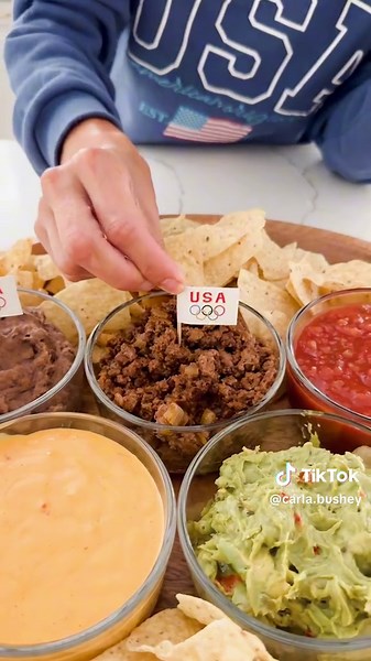 Make this for an olympics watch party. You will need 5 bowls of the same kind to make the circles. I also added some Olympics flags for an extra touch. Mine are linked on my LTK shop in by-oh You will add to each bowl: 1. Nacho Cheese (I used Tostitos brand and warmed it up) 2. Guacamole (homemade or store bought) 3. Salsa 4. Seasoned taco meat (I cooked 8oz of ground beef with onions and a pack of taco seasoning) 5. Refried black beans (I got a can of Goya refried black beans and add a little s