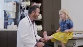 A caring male pediatric orthopedist tickles a young patient's foot to...