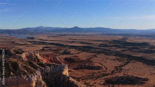High altitude footage overlooks a vast primeval landscape leading to a monumental distant peak. The sun-scorched badlands and deep shadows create a powerful and universal alien planet background.