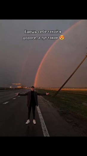 Man Standing on Road Under a Vibrant Rainbow