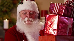Santa Claus peeks out from behind stack of gifts