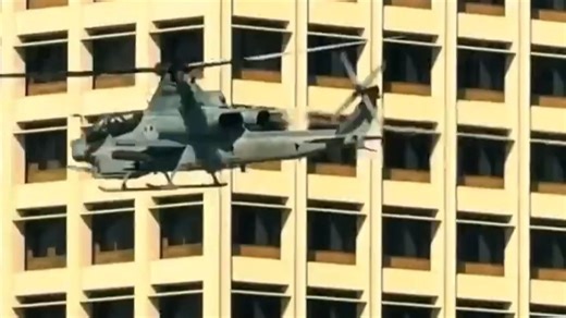 美国海军陆战队的一架 AH-1Z 攻击直升机飞过洛杉矶市中心，挂架上挂载了“九头蛇”火箭弹或“陶式”导弹。