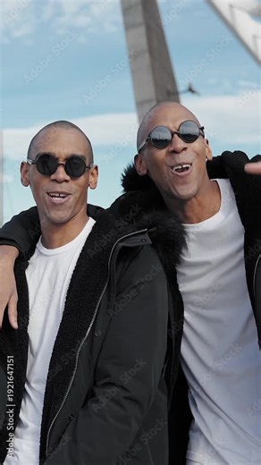Two cuban twin sibling rappers are singing and dancing, wearing sunglasses and winter jackets
