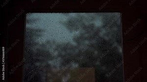 Raindrops dripping on a window with a storm outside in dark weather