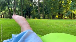 A woman wiggles her bare toes against the background of green grass in a summer park. Outdoor recreation.