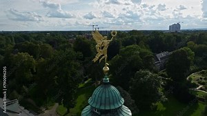An aerial drone shot captures a golden statue atop the University of Münster , Westfälische Wilhelms-Universität-Münster in Germany .