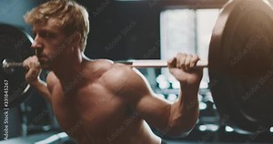 Strong muscular man working out doing barbell squats in the gym as part of his fitness routine, man with an amazing body sculpted by determination and focus