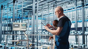 Senior engineer in smart photovoltaics factory looking at system performance metrics on tablet. Experienced solar panels plant worker tracking energy production through IoT sensors on device, camera A