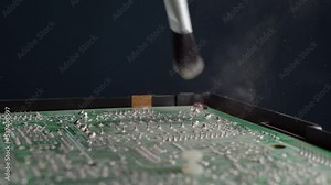 Close up worker in an electronics service center removes dust from an old large chip. Cleaning electronics box with brush, the dust rises when cleaning electrical circuit board.