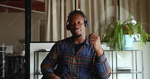 African man sitting at workplace wear headphones looks at camera start videocall communication. Online class participant, streamer attendee use video conferencing application, virtual meeting concept