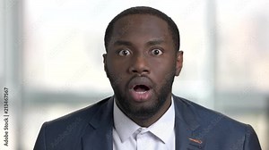 Portrait of shocked afro american business man. Surprised and shocked face of black man in suit, close up. Bright office, windows background.