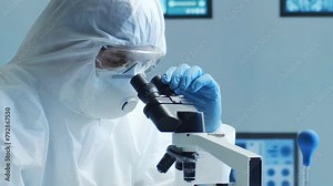 Scientist in protection suit and masks working in research lab using laboratory equipment: microscopes, test tubes. Medicine, healthcare and technology concept.