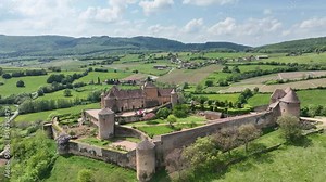 Aerial panning shot of Berze le chatel feudal medieval castle with double enclosure of walls, round towers, donjon, fortified gatehouse on a hill in Central France