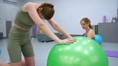 Woman performing flexibility exercise on green stability ball in gym...