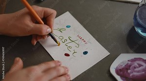 Close-up. Woman hands painting eggs on an Easter greeting card with a brush with yellow watercolor paint. DIY Easter card