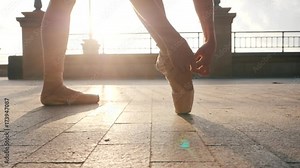 Close up of a ballet dancer's feet as she corrects pointe on the stone embankment. Woman's feet in pointe shoes. Ballerina preparing for classic ballet pas. Slow motion. Flare, gimbal shot