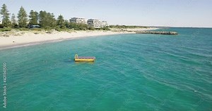 Tourists Swimming On Blue Sea With Floating Swim Platform With Beach And Hotels In background In Perth, Western Australia. - aerial