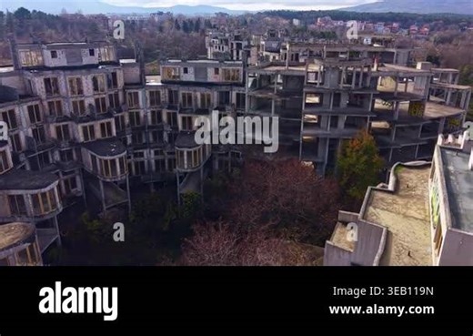 Desolate buildings rise against a backdrop of trees, showcasing crumbling architecture where nature begins to reclaim its space. A haunting yet captivating view of urban abandonment Stock Video Footage - Alamy