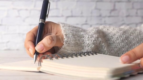 Woman writing in notebook with pen on wooden table