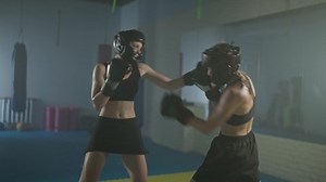 Sparring fight of two female fighters wearing protective helmets, training in the boxing gym, females train defence and series of punches on a battle.