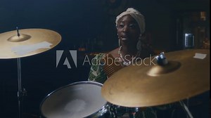 African American female young vocalist playing guiro and singing during rehearsal with unrecognisable Black male drummer