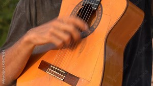 Man musician playing of a acoustic guitar on the beach at sunset in island Koh Phangan, Thailand. Male hands playing on the strings of a guitar, close up