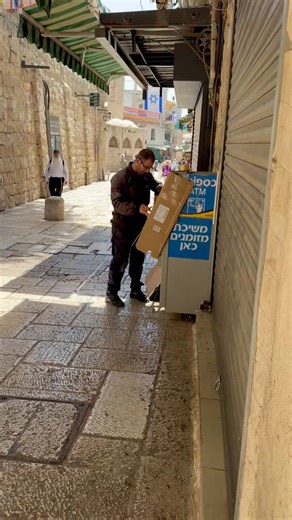 A Jewish man prepares his ATM machine ahead of the thousands of Flag Day participants who will march through the Muslim Quarter, wrapping it in cardboard and writing the words, “This belongs to a Jew. Do not damage. Thanks.”