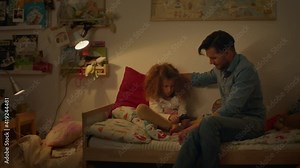 Pretty Eight Year Old Girl Sitting On The Bed And Looking At Pictures. Child Is Sad. Young Dad Sits Down Next To Girl. Daughter Hugs Dad.