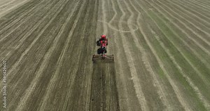 Field works. Tractor sowing seeds with seeder driller in field. Process of sowing cereals and other crops. Sowing work in the field. Tractor with seeder performing seeding. Top down drone view.
