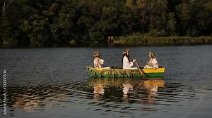 Three young girls with long hair in a boat floating on the river. Girls rowing oars on the water.