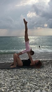 Mother and daughter practicing yoga togetherness at sea, seaside. Woman and child girl practice acrobatic and gymnastic exercise - handstand, balance