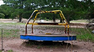 An old rusty and abandoned merry-go-round toy spinning with no one in it outdoors.