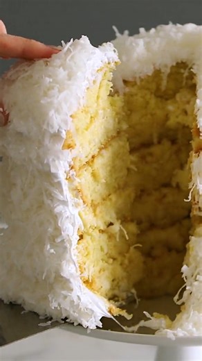 This cake is a coconut lover's dream. It's a towering creation of six tender cake layers sprinkled with shredded coconut and filled with a rich coconut custard. Frosted with mountains of billowy seven-minute frosting, it becomes even taller. Get the recipe: bit.ly/4aRJ3jJ | Martha Stewart