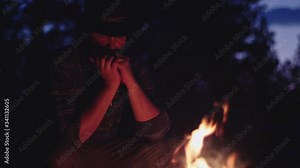 Cowboy plays the harmonica by a campfire at night in slow motion