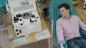 Tracking shot from above of two young men talking on medical chairs in blood donation center. One man donating blood with mega platelet machine separating plasma and blood cells