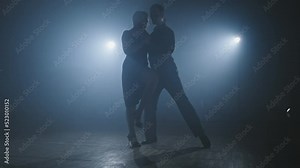 Young couple dance tango in dark room with smoke and spotlights in slow motion. Silhouette of dancers in smoky ballroom. Wide angle in 4K, UHD