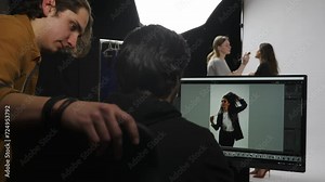 Model and production team in the studio. Editor and photographer discussing photos looking at monitor, girl assistant fixes model makeup.