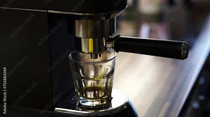 A closeup of a coffee machine engineering the perfect cup of coffee. The liquid is poured into a glass through the metal rim, showcasing the intricate process of this kitchen appliance