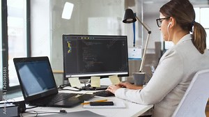 business, programming and technology concept - female programmer in earphones working with script on computer screen and listening to music at office