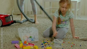 mom and daughter, a young woman cleans up with a vacuum cleaner, a little girl with blond hair collects toys, the designer in a container, helps mom